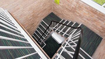 A brick-walled stairwell with a metal handrail and a yellow sign indicating directions to reception, lounge, and dining areas.