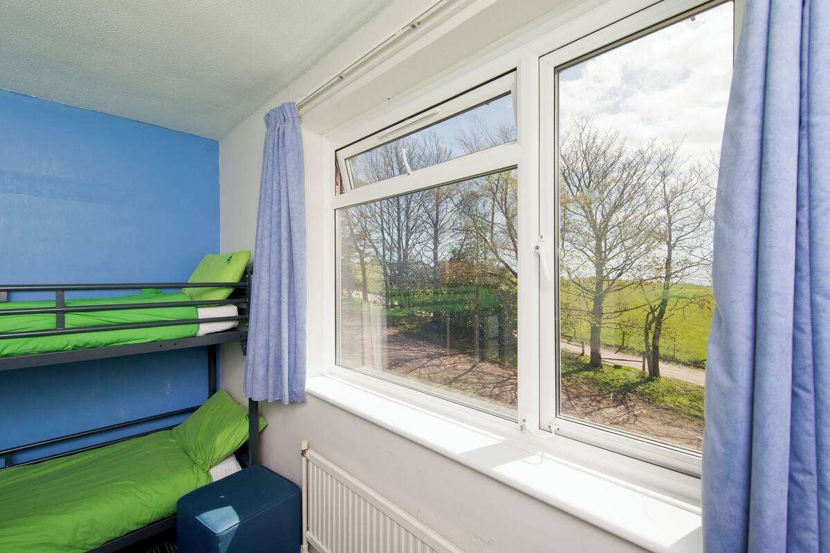 Une chambre avec un lit superposé et une fenêtre donnant sur un paysage rural.