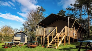 Een camping met een houten hut, een campers met luifel en picknicktafels.
