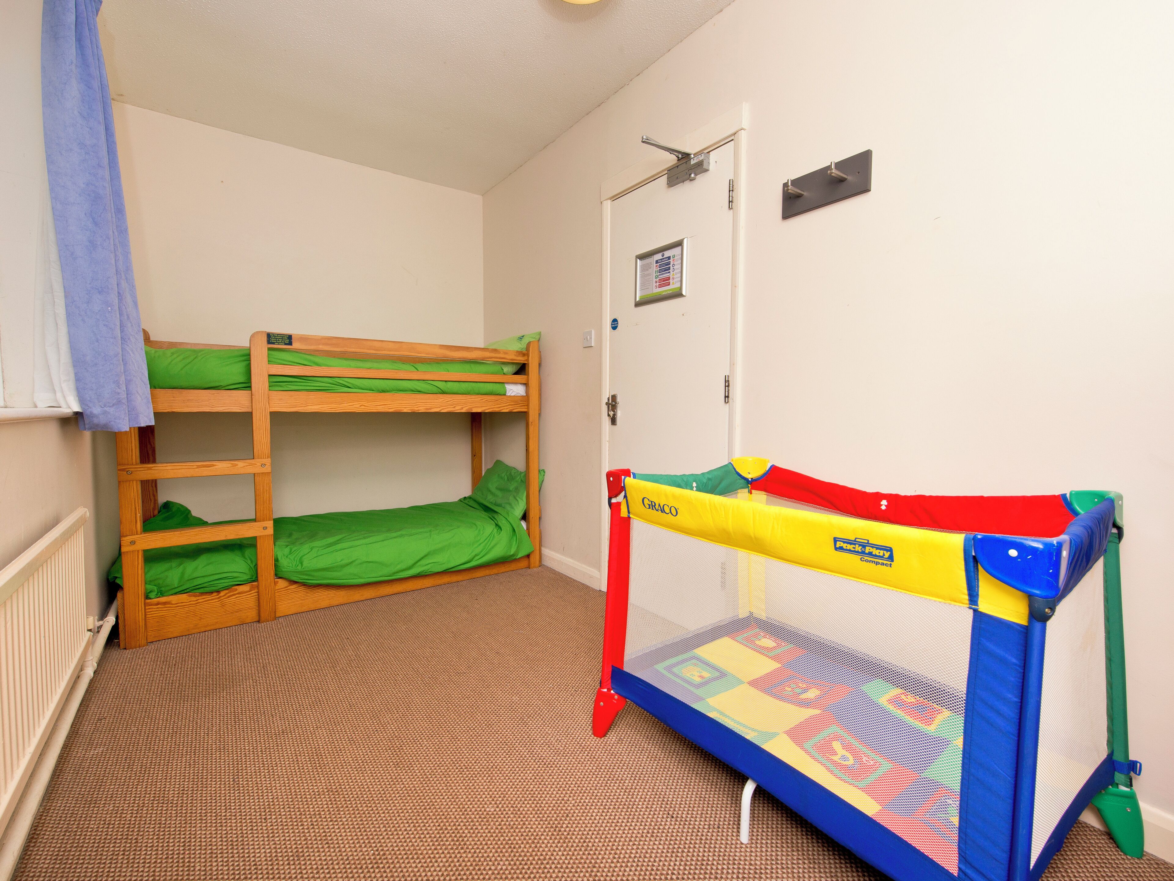 A bunk bed room with a playpen and a door with a notice.