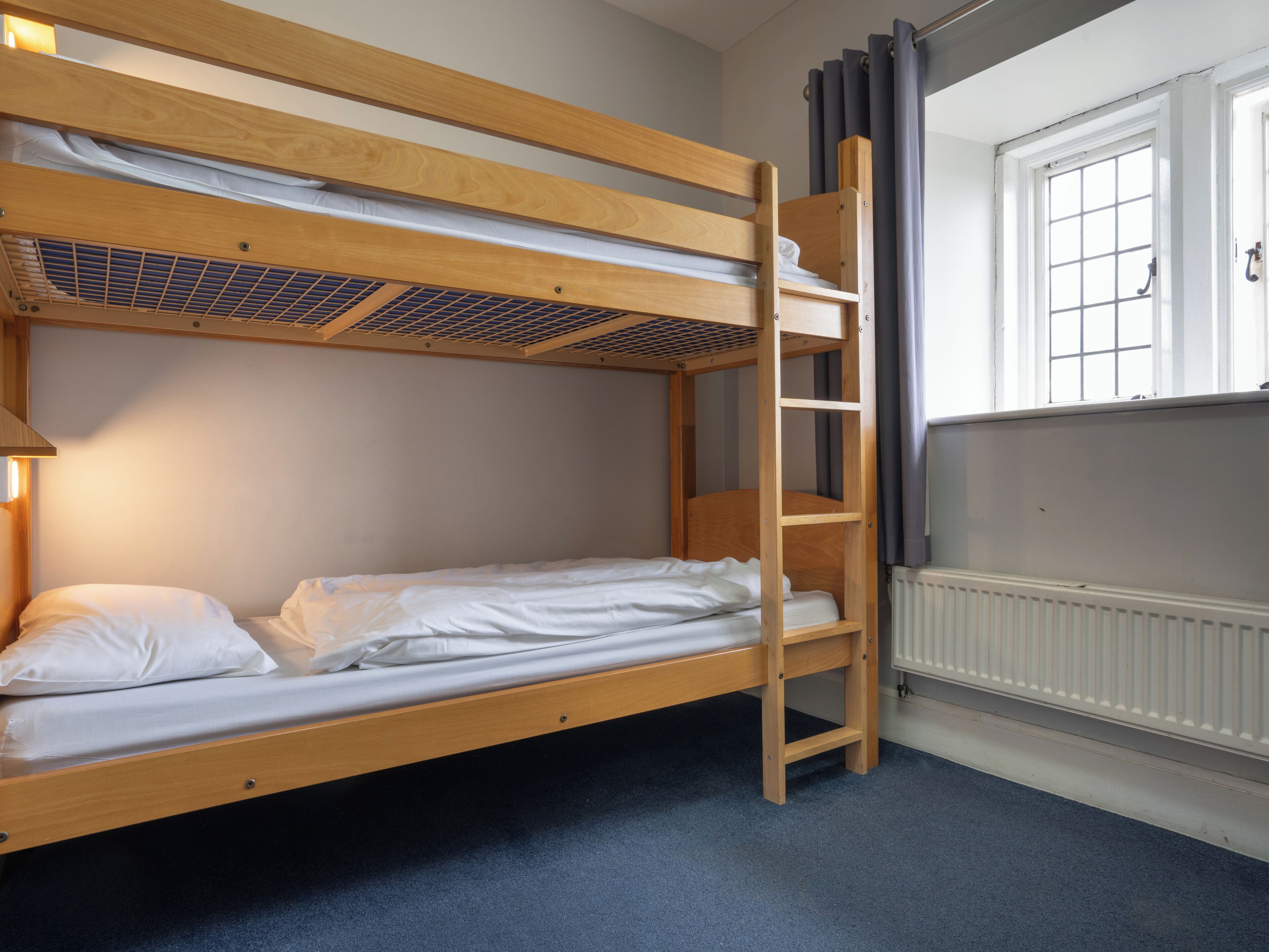 A bunk bed with a ladder, white bedding, and a window with curtains.