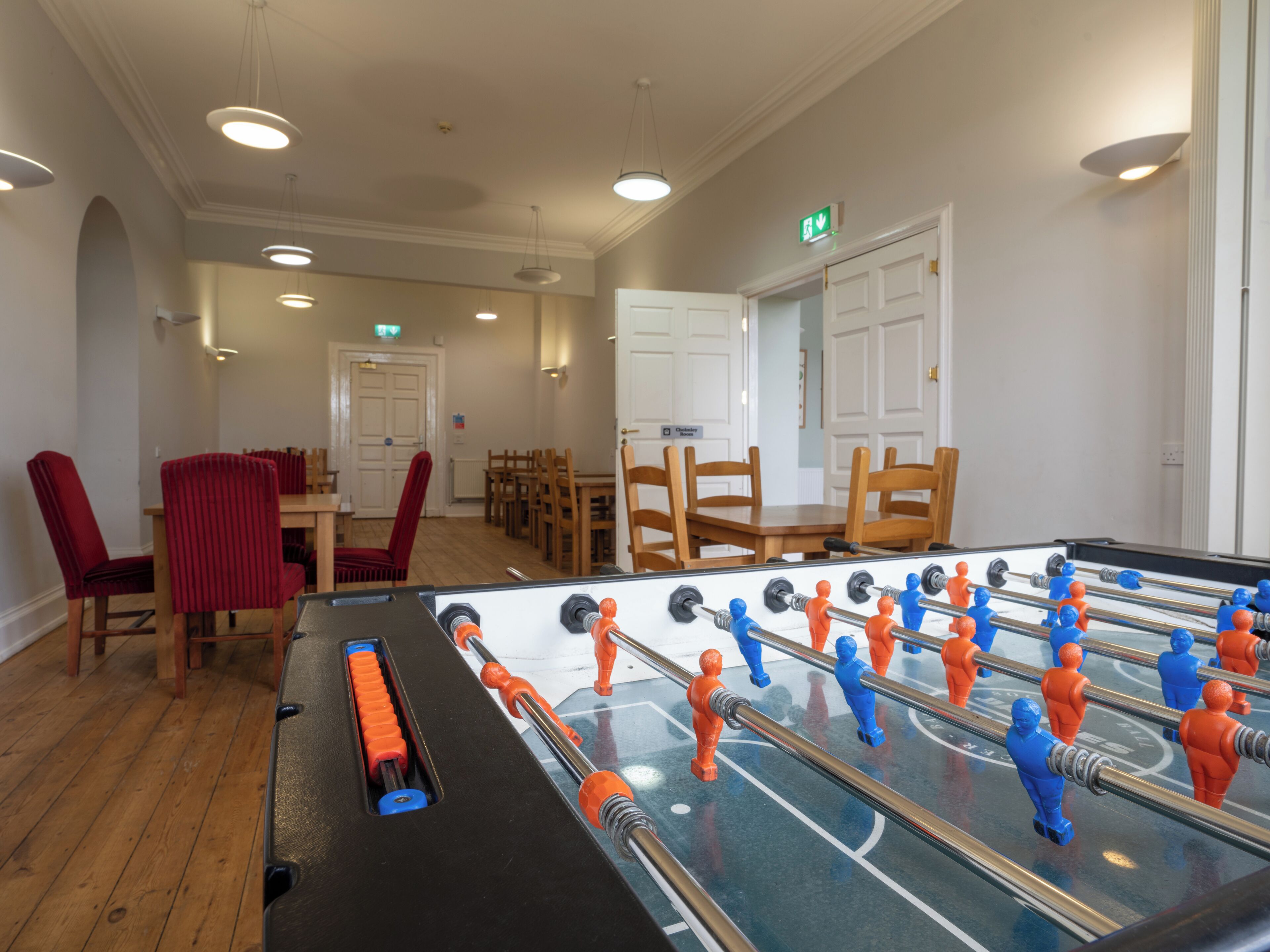 A room with a foosball table, wooden chairs, and a dining table with chairs.