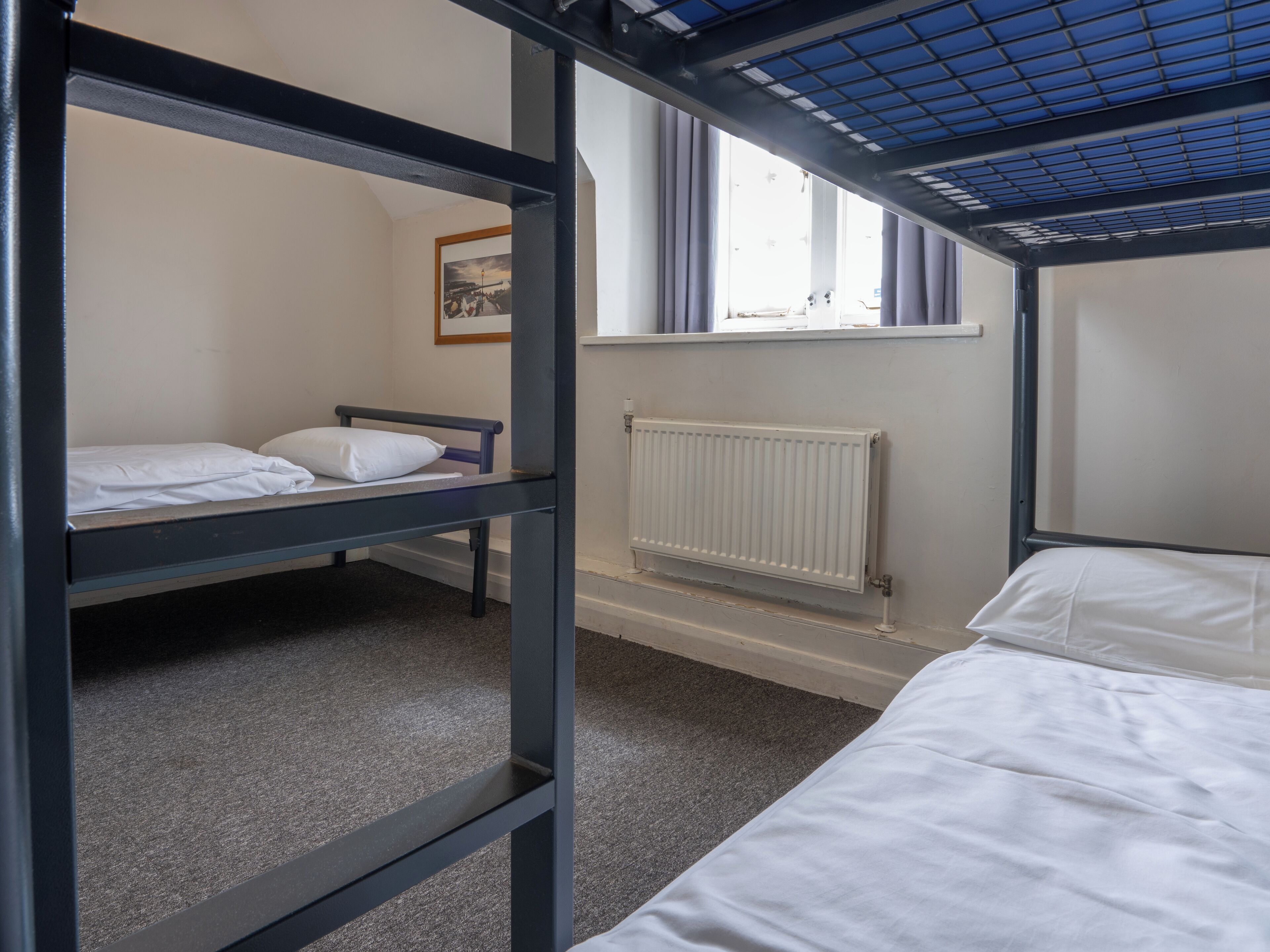 Een slaapzaal met stapelbedden, een radiator en een raam met gordijnen.