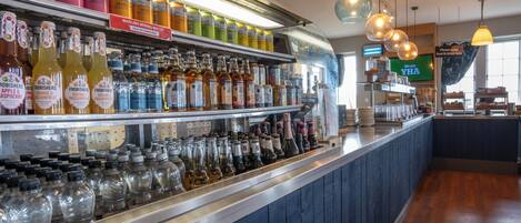 A bar area with shelves stocked with various bottles and glasses, a counter with a menu, and hanging pendant lights.