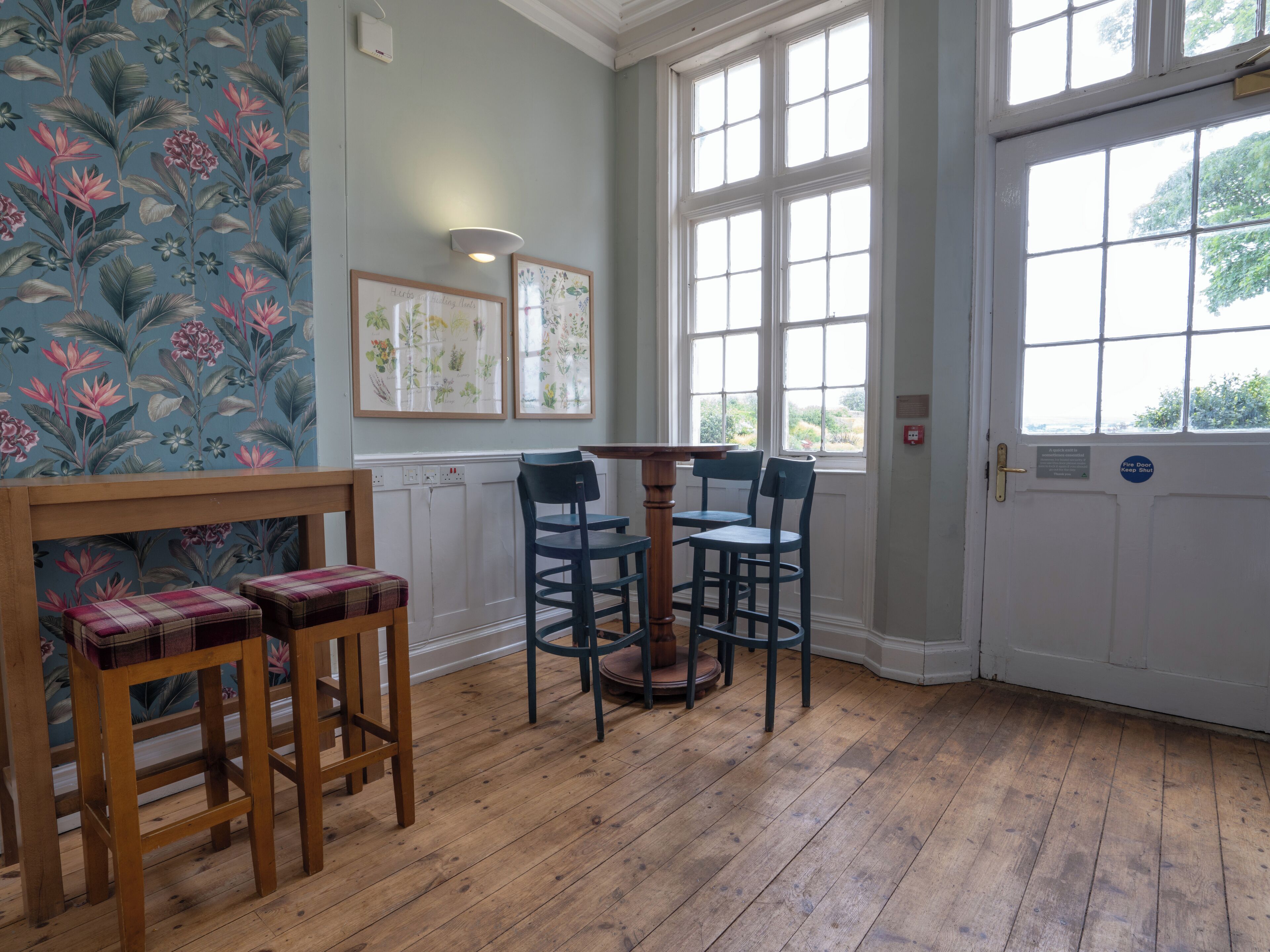 A room with a wooden floor, a table with chairs, a door with a sign, and floral wallpaper.