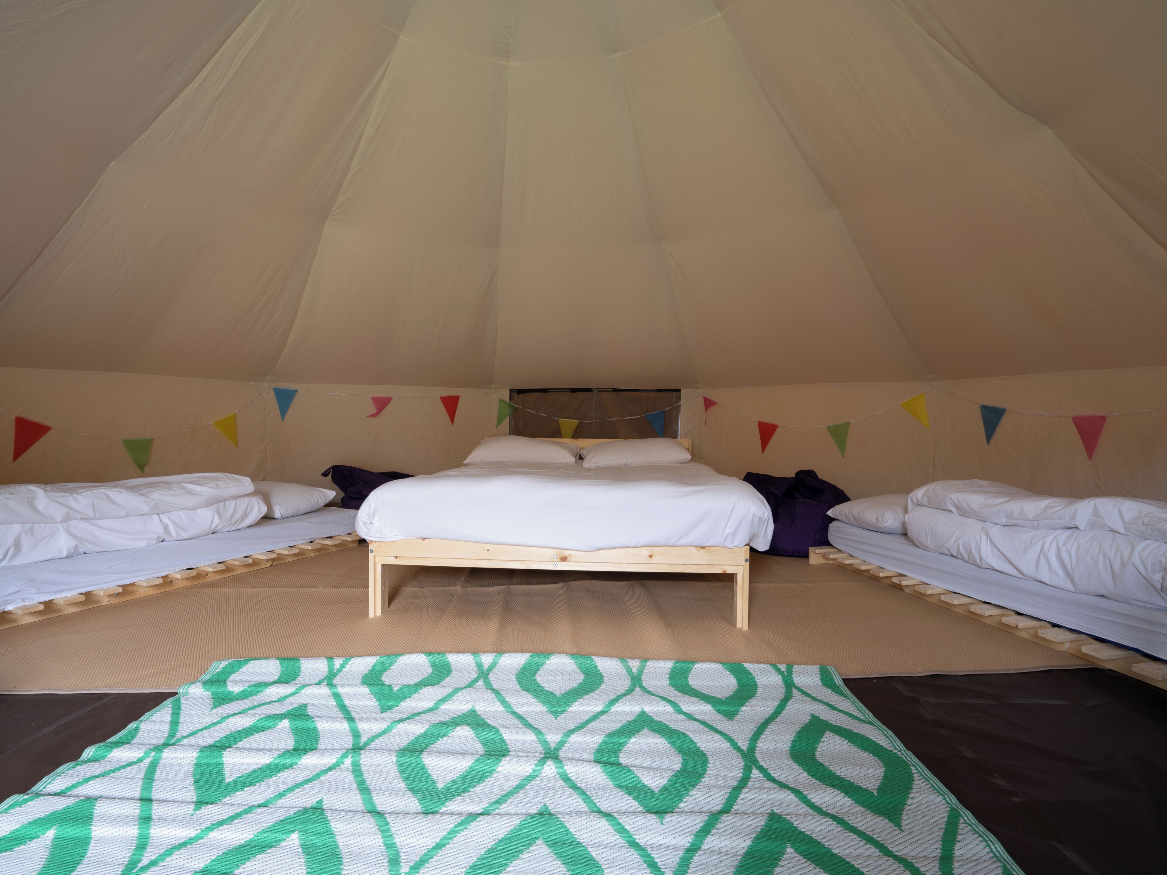 Una carpa con una cama individual y dos camas más pequeñas, coloridas banderas triangulares y un tapete estampado.