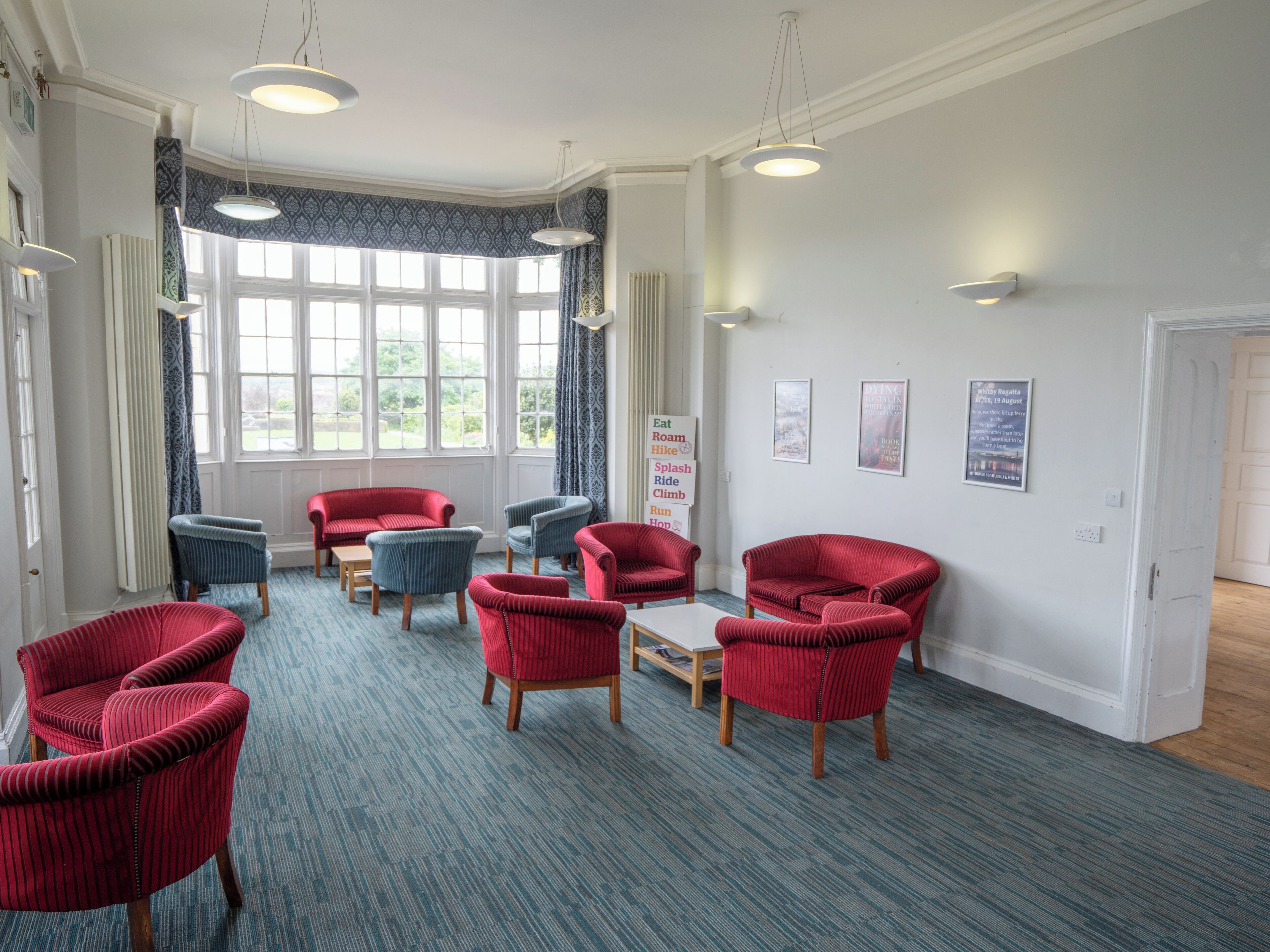 A room with red and blue upholstered chairs, a small table, and a window with patterned curtains.