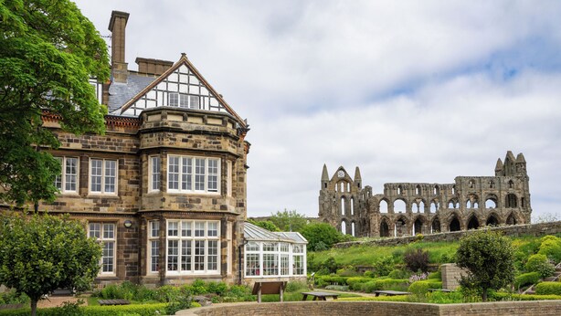 A historic building with a large garden and a ruinous structure in the background.