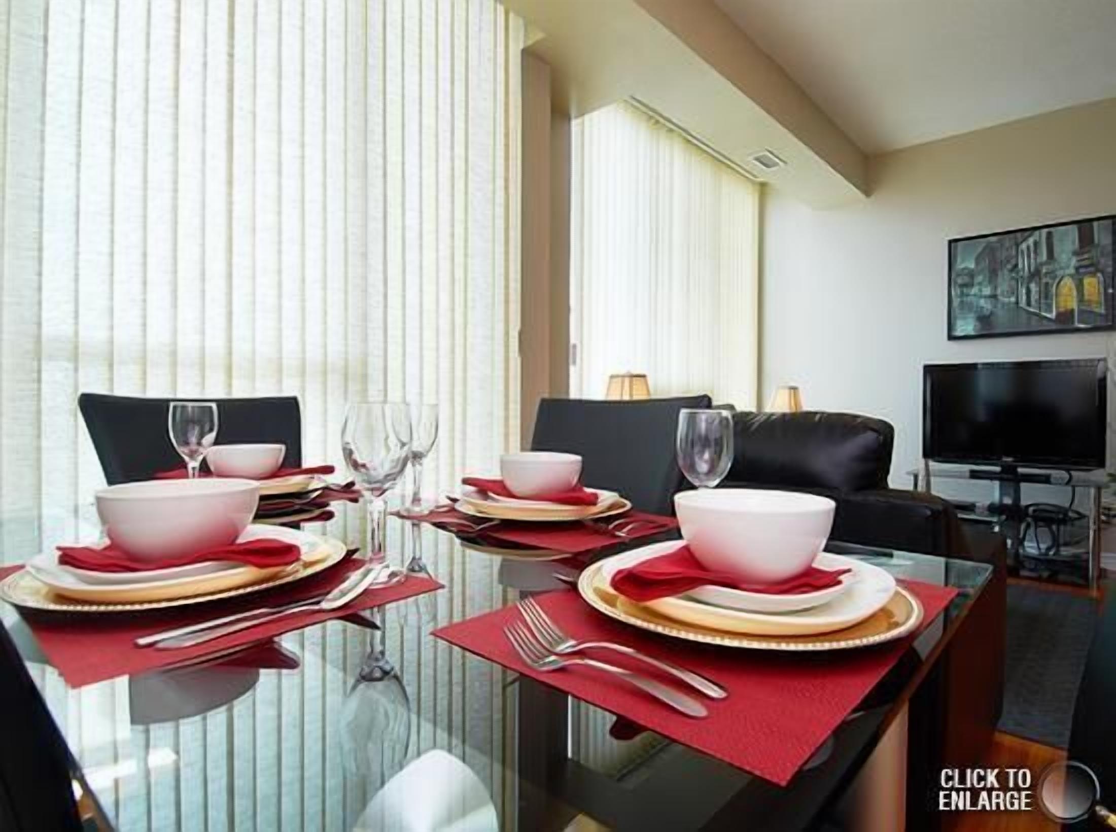 A dining area with a glass table set for two, red napkins, and a black leather couch in the background.