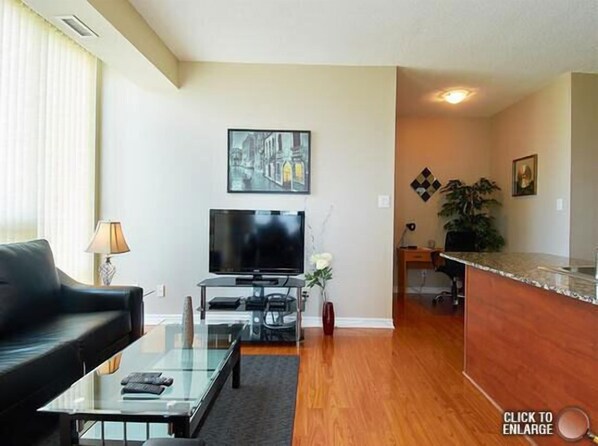 A modern living room with a flat-screen TV, a glass coffee table, and a black sofa.