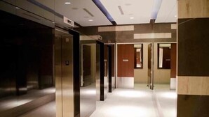 Un pasillo moderno de hotel con ascensor central, varias puertas y un interior limpio y bien iluminado.
