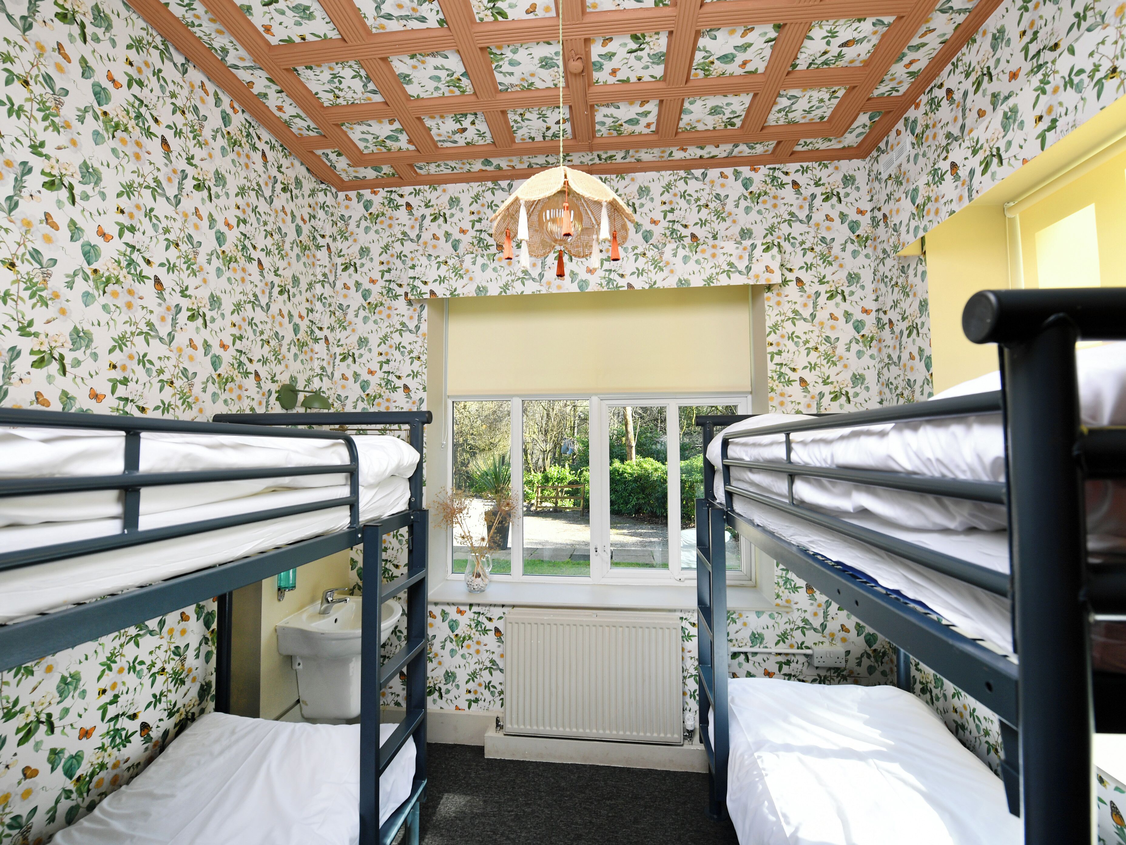 A dormitory room with bunk beds, a window, and floral wallpaper.