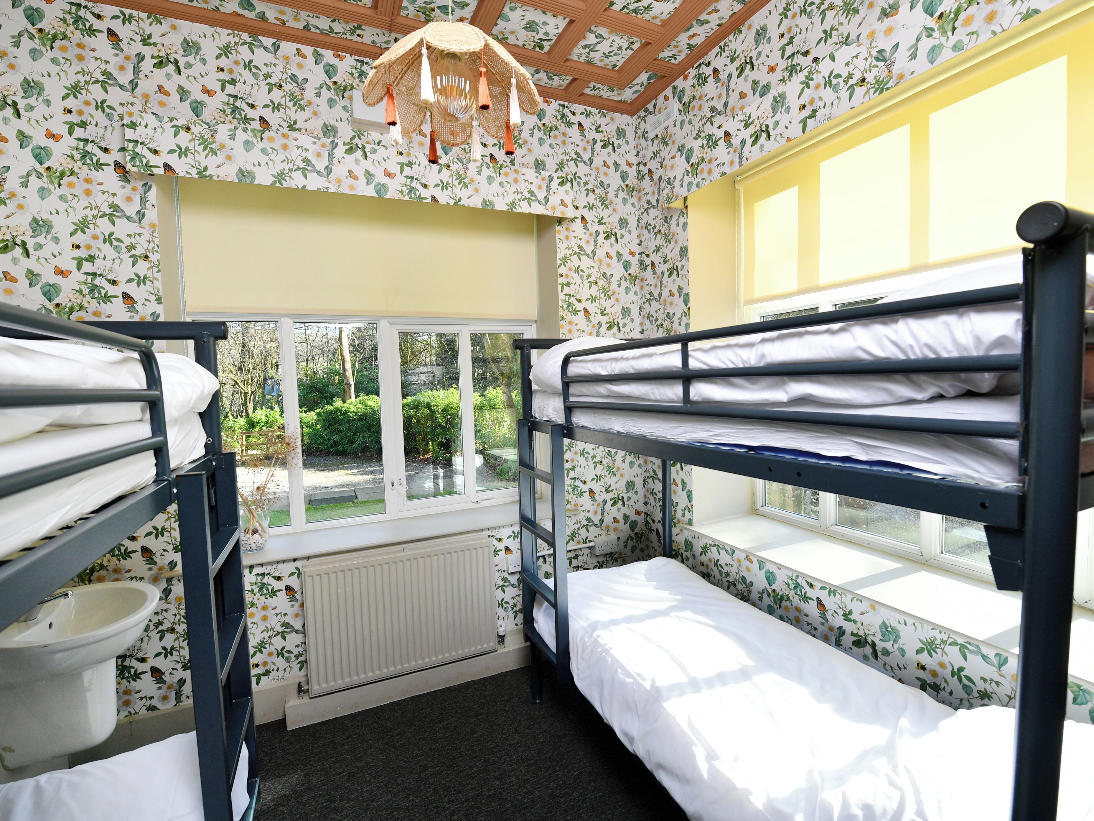 Un dormitorio con literas, una ventana con vistas a la vegetación, un radiador y una lámpara colgante.