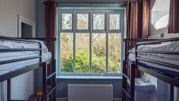 A dormitory room with bunk beds, a window with curtains, a radiator, and a sink.