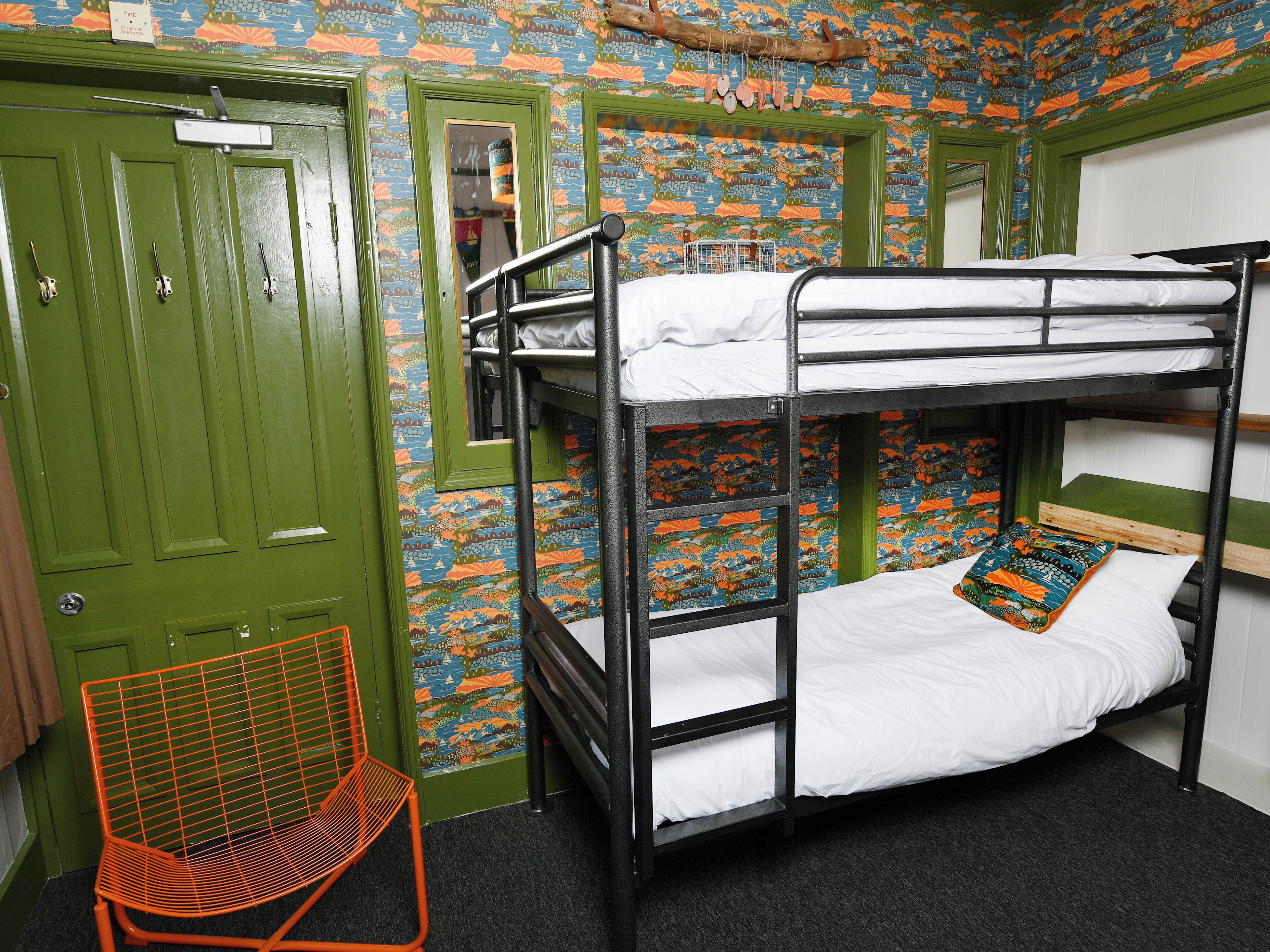 A bunk bed room with green doors, patterned wallpaper, and a metal chair.