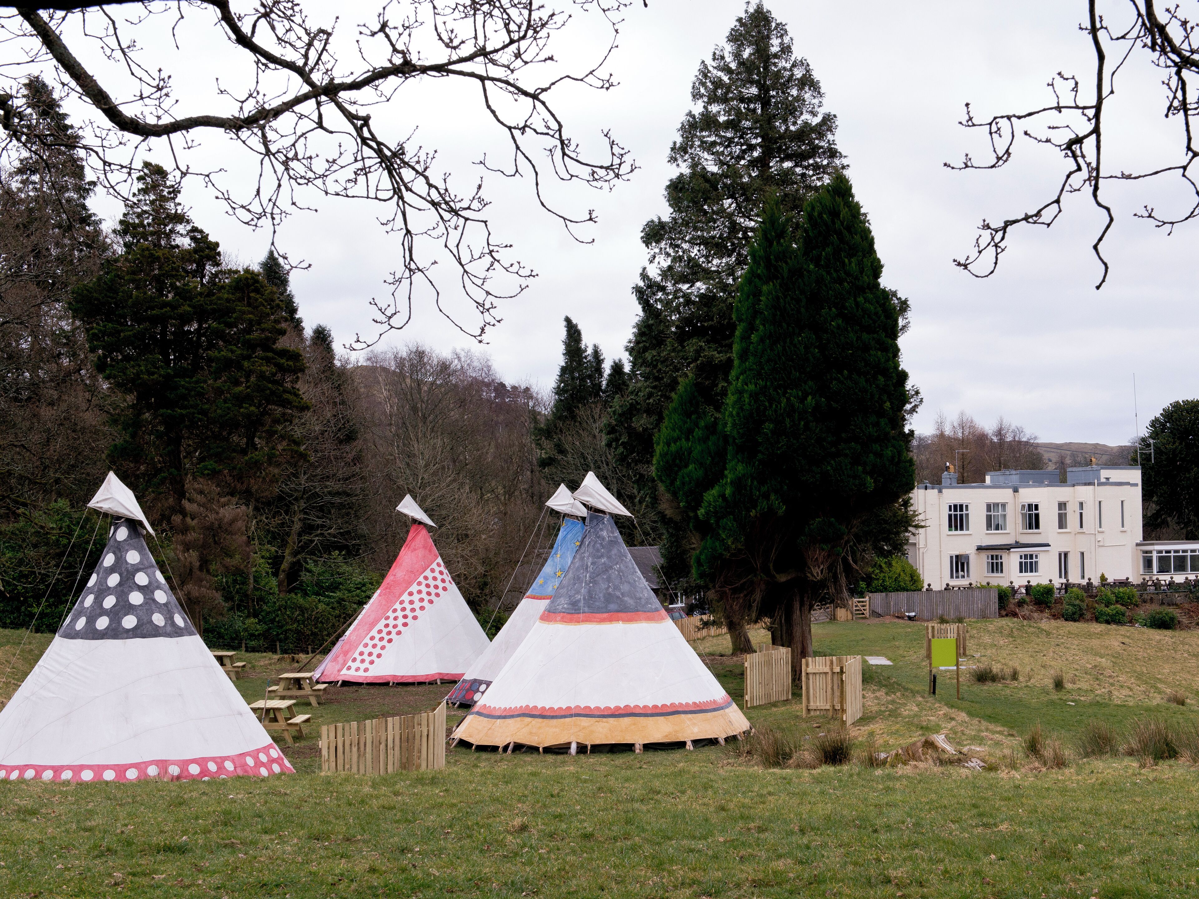 Three tipi-style tents in a grassy area with a building in the background.