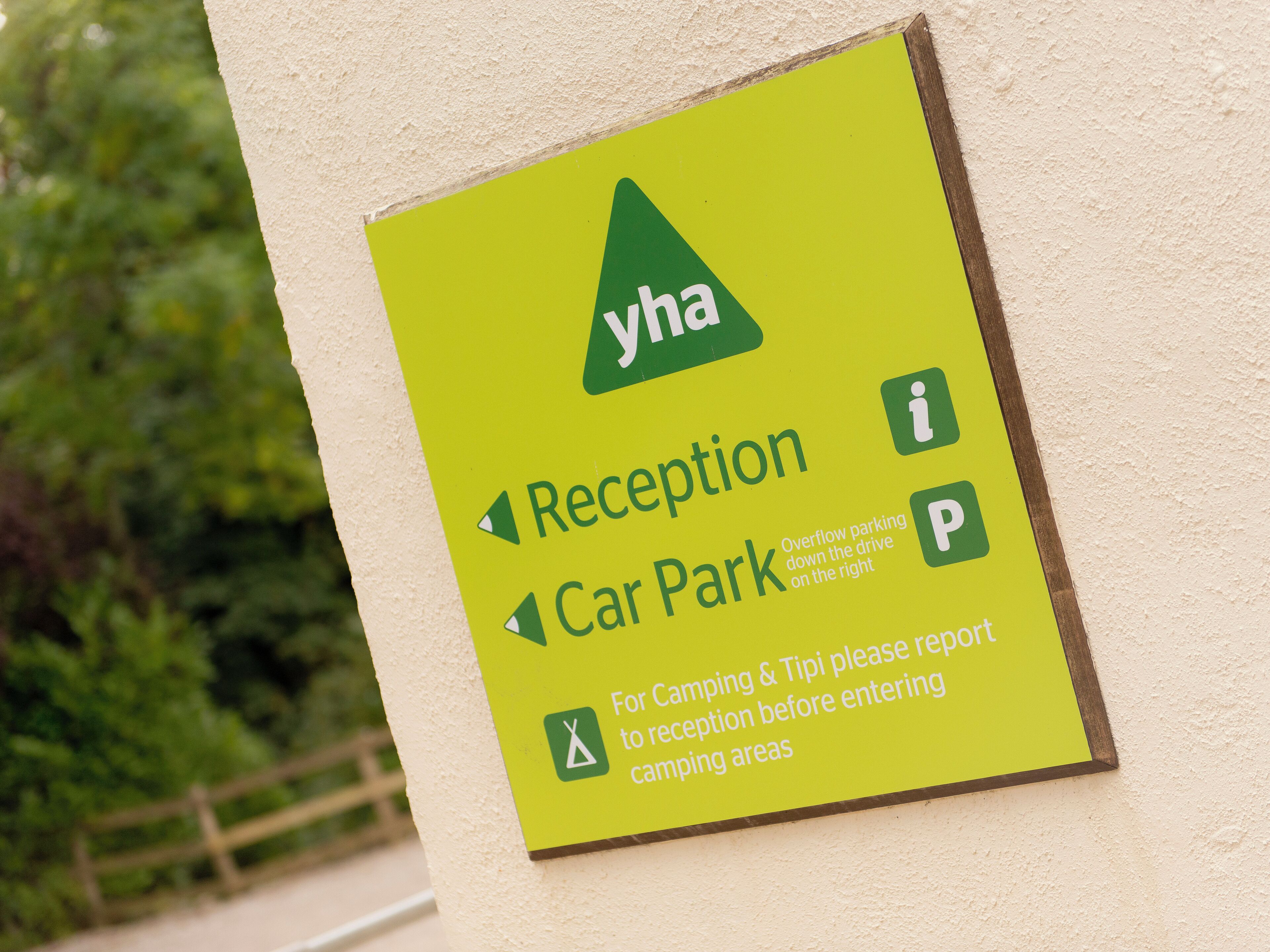 Un letrero con el logotipo de YHA, que indica la zona de recepción y aparcamiento. También indica que para acampar o usar tipis, hay que informar en recepción antes de acceder a las áreas de camping.