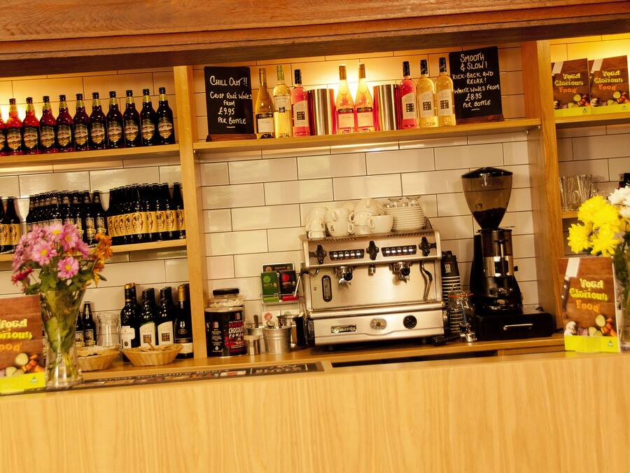 A bar area with a coffee machine, shelves of bottles, and a sign indicating food and drink prices.