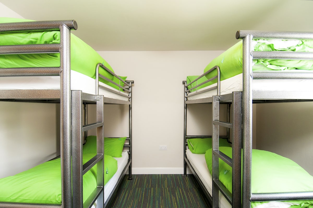 A room with bunk beds, each with green bedding and pillows.