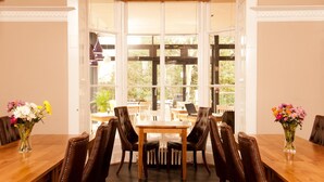 A dining area with a large table and chairs, a view through a glass door to an outdoor seating area, and a vase of flowers on the table. - YHA York - Hostel (York)