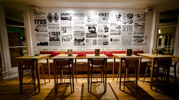 Un restaurante con una larga pared que exhibe fotografías e imágenes históricas. Hay mesas de madera y asientos tipo banca con cojines rojos.