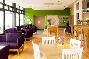 Un hall d’entrée moderne avec des sièges violets, un comptoir d’accueil en bois et un mur d’accent vert.