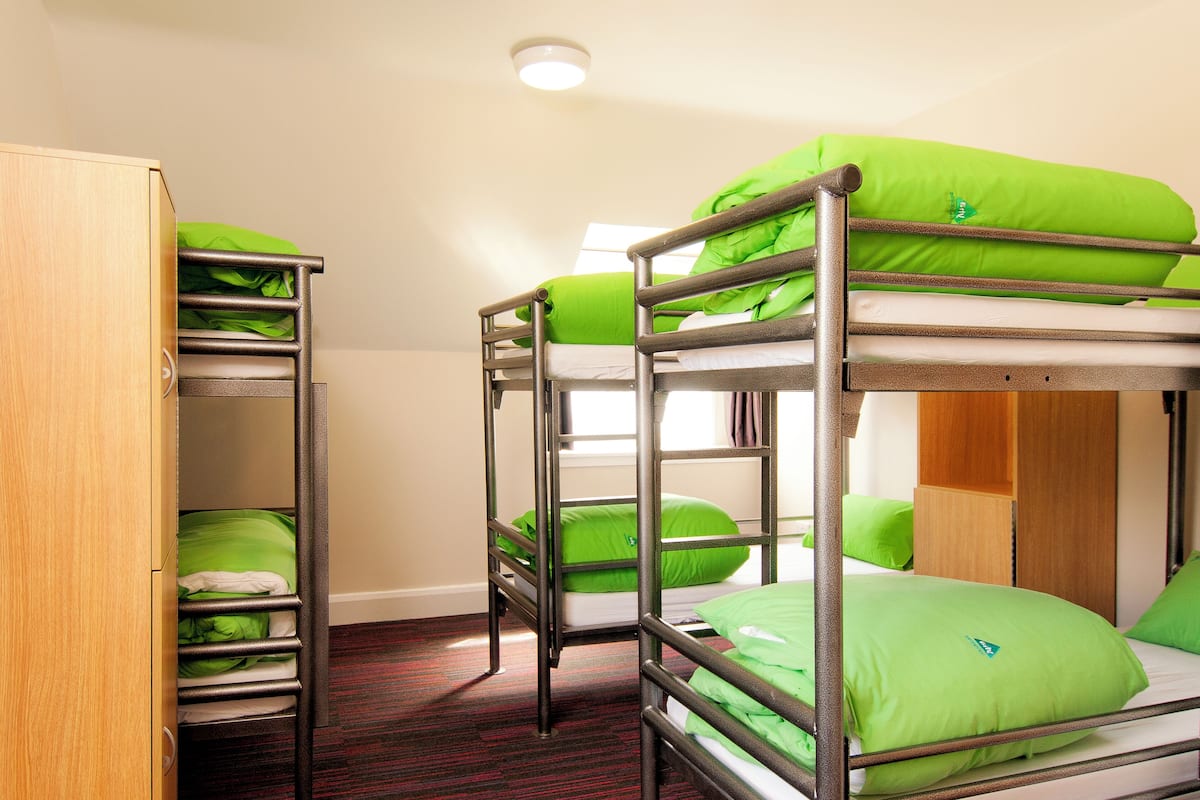 A bunk bed room with green bedding and a wooden wardrobe.