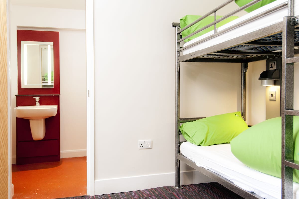 A bunk bed with green bedding, a red sink, and a mirror above it.