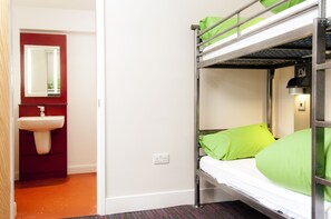 Un lit superposé avec une literie verte, un lavabo rouge et un miroir au-dessus.