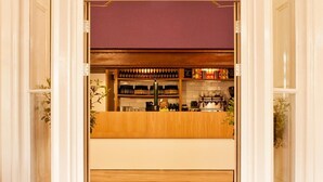 A bar area with wooden flooring and white walls, featuring a purple backdrop and shelves with bottles. - YHA York - Hostel (York)