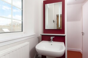 Une salle de bain avec un lavabo blanc, un miroir et une fenêtre.