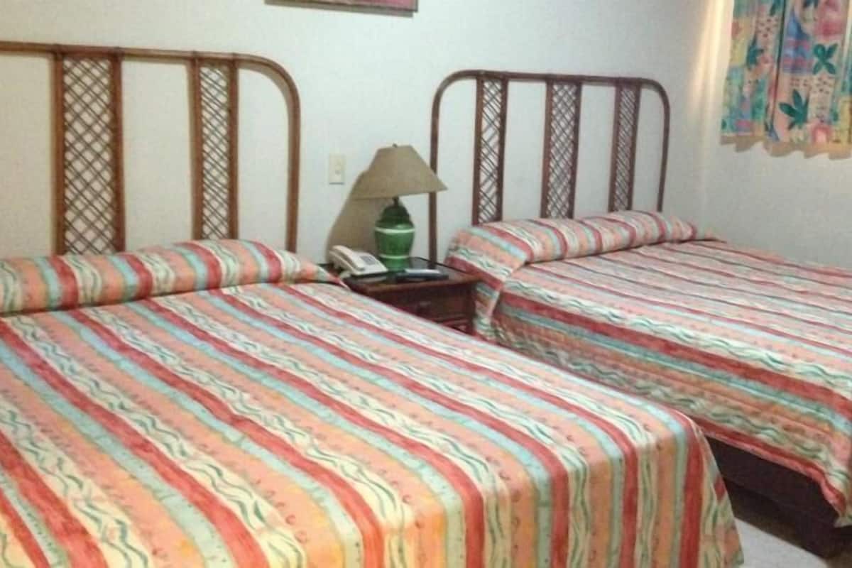 Une chambre avec deux lits simples, dotée de draps à rayures, d’une table de chevet avec une lampe et d’un mur sur lequel est accroché un rideau.