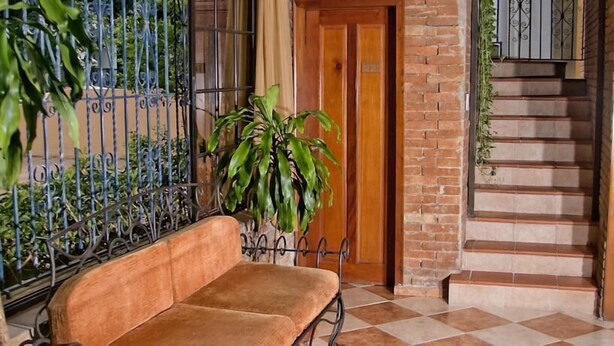 Un espacio interior acogedor con un banco de madera, una planta en maceta, una reja de metal y una escalera.