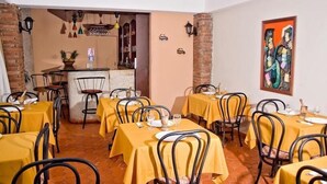 Un restaurante con manteles amarillos y sillas de metal, que presenta una pared de ladrillo y un cuadro en la pared.