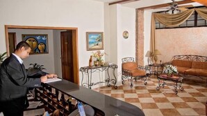Un hombre en la recepción de un hotel, con suelo a cuadros, un sofá, una mesa de centro y objetos decorativos en una mesita.