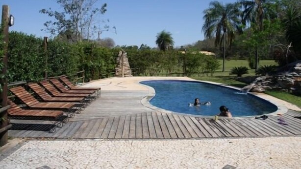 A swimming pool with wooden deck chairs and a sandy area. - Pousada Moinho de Vento (Bonito)
