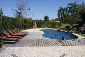 A swimming pool with wooden deck chairs and a sandy area. - Pousada Moinho de Vento (Bonito)