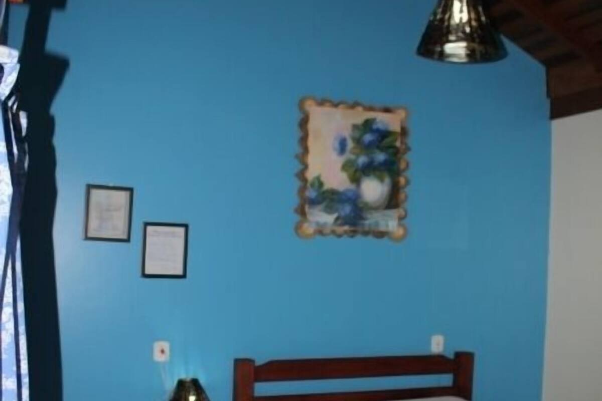 Une chambre avec un mur bleu, un cadre de lit en bois, une couvre-lit bleue, une petite table de chevet avec une lampe et un tableau encadré accroché au mur.