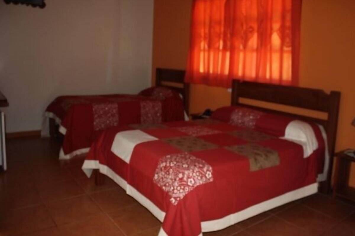 Une chambre avec deux lits simples, une tête de lit en bois et un rideau rouge.