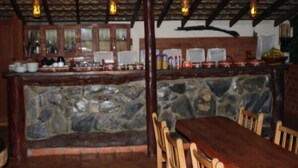 A stone bar area with wooden chairs and a long table, surrounded by kitchen cabinets and a stone wall. - Pousada Moinho de Vento (Bonito)