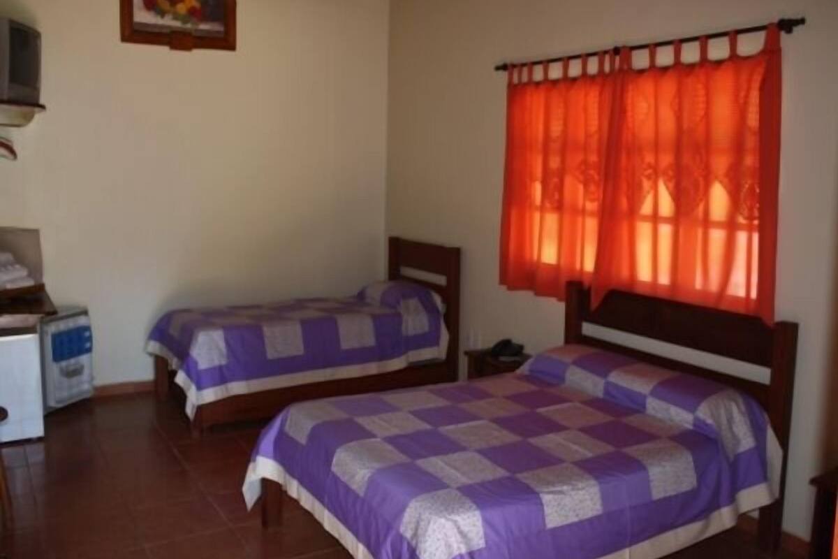 Une chambre avec deux lits, une petite table, un téléviseur et une fenêtre avec des rideaux orange.