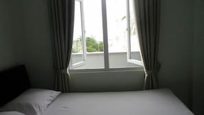 Een hotelkamer met een bed, een raam met gordijnen en uitzicht op groen.