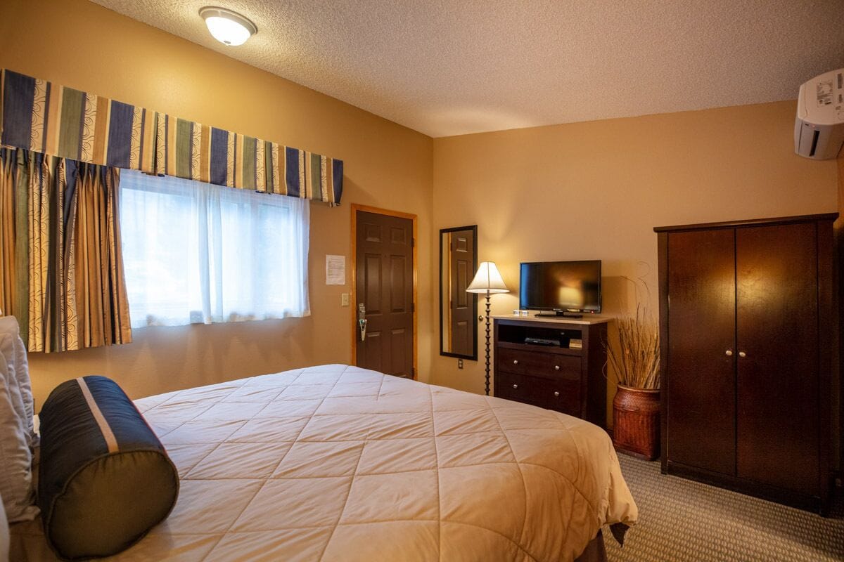 A hotel room with a large bed, a television, a desk, and a wardrobe.