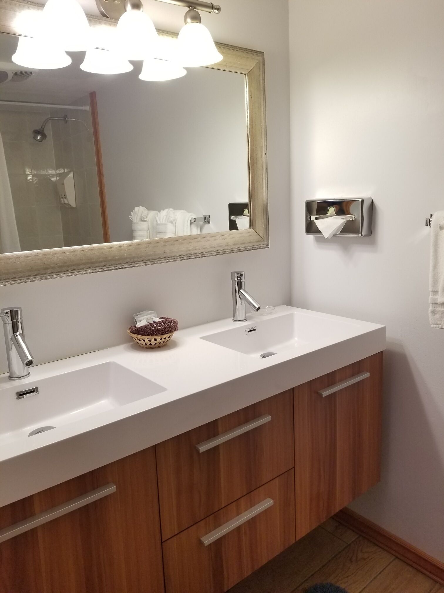 A bathroom with two sinks, a mirror, and a towel dispenser.
