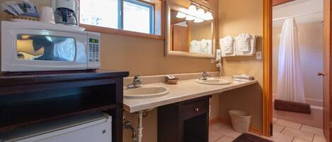 A bathroom with a microwave, two sinks, a large mirror, and a shower curtain.