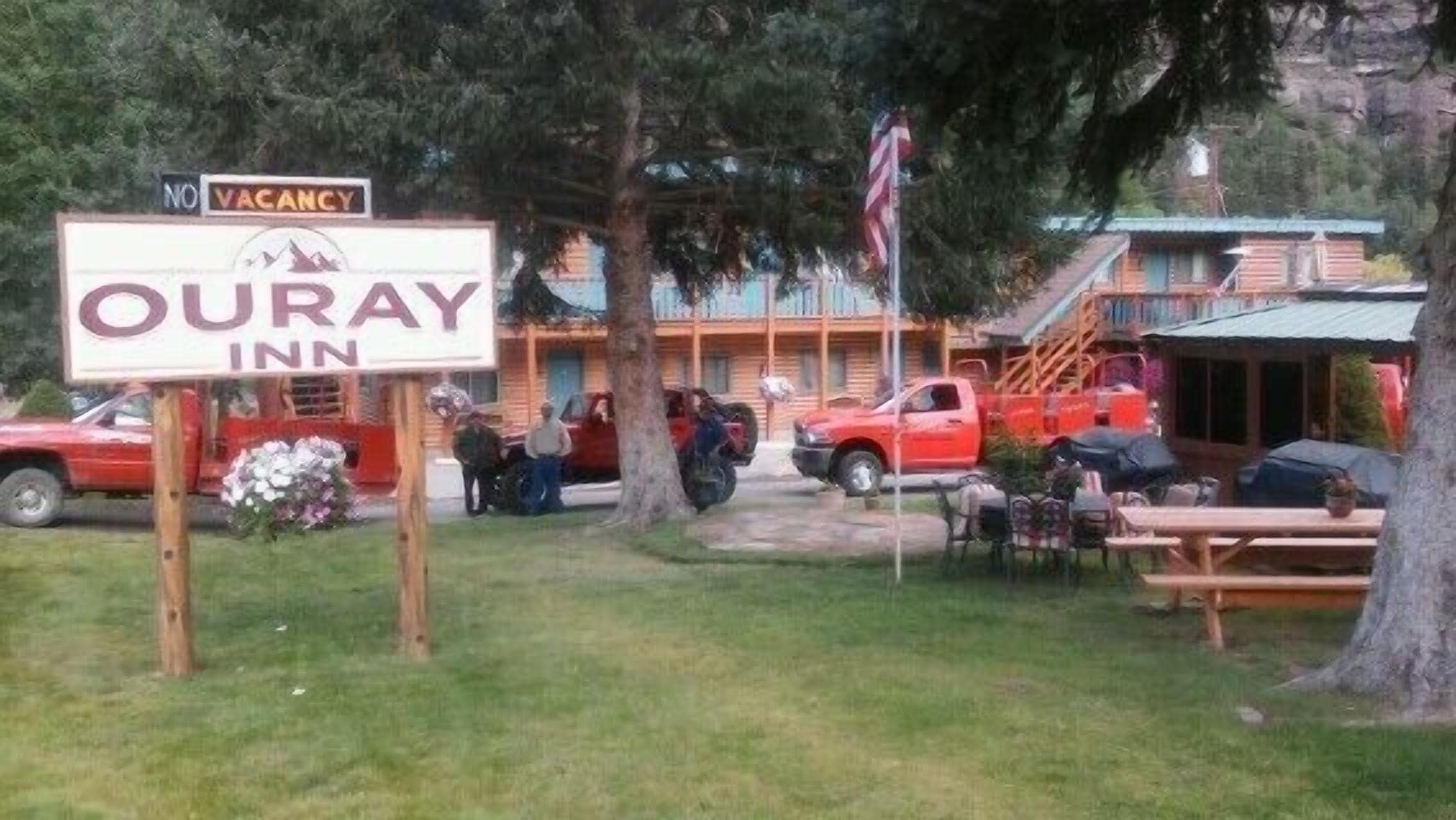 A sign for Ouray Inn with a 'No Vacancy' notice, outdoor seating, and a red vehicle parked nearby.