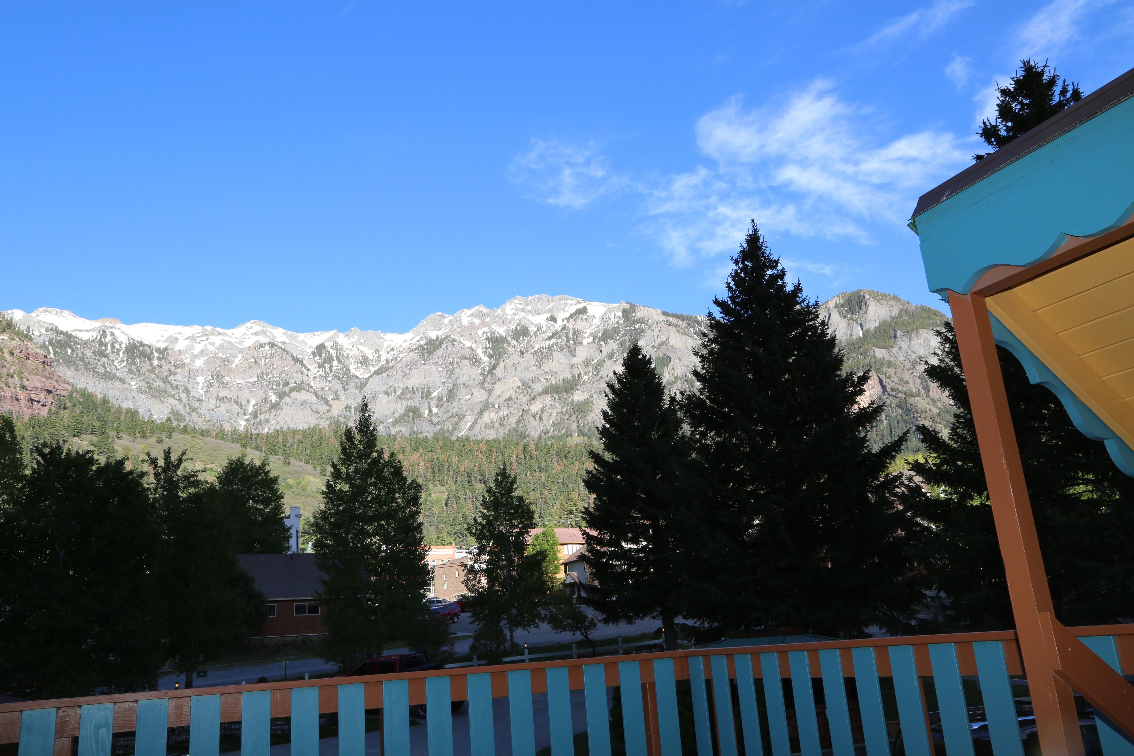 A mountain view with a wooden fence in the foreground, a building with a blue roof, and a clear sky.