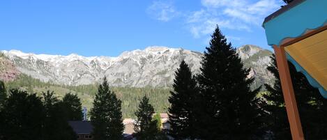 A mountain view with a wooden fence in the foreground, a building with a blue roof, and a clear sky.