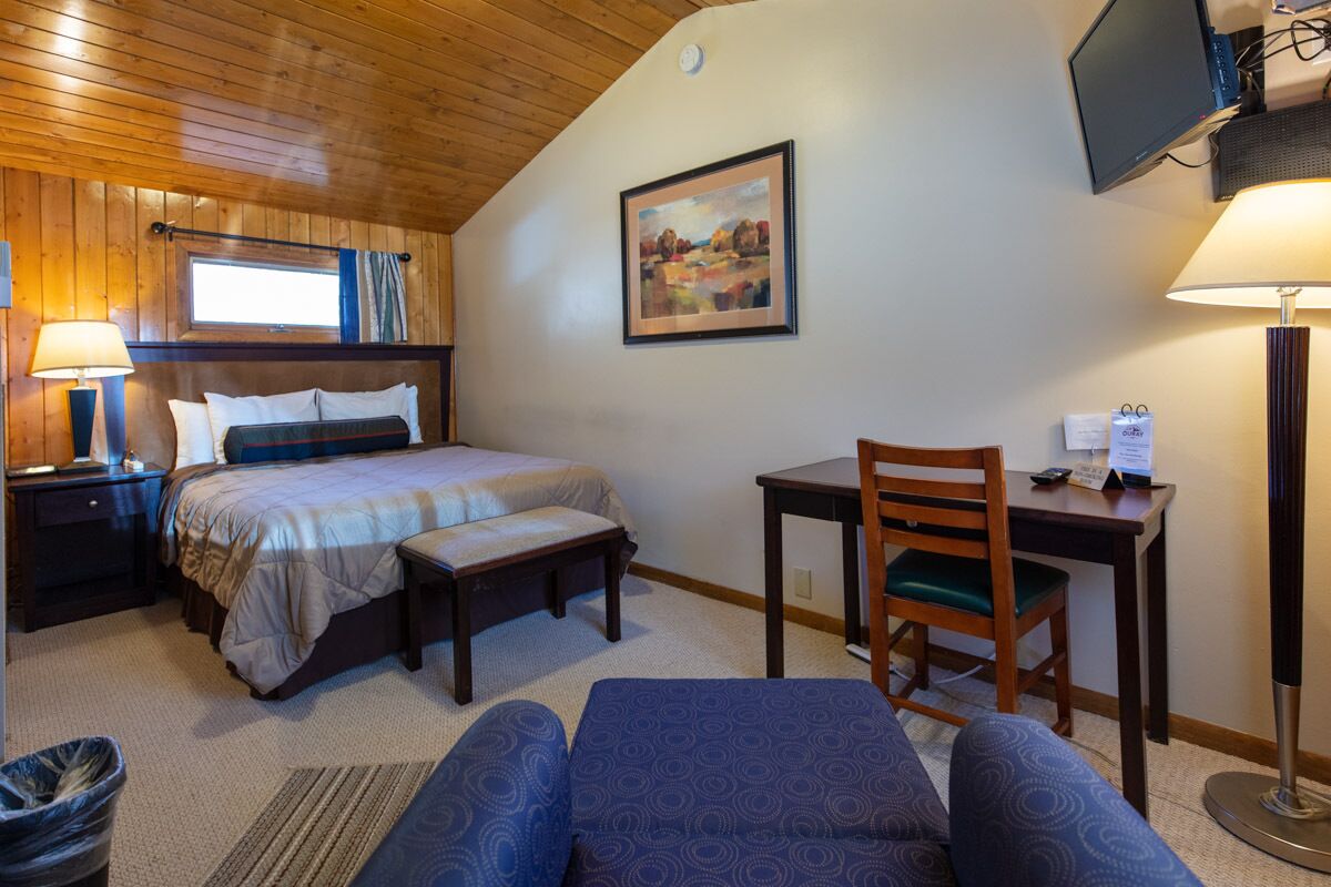 Une chambre à coucher avec un lit, un bureau, une chaise, une lampe et un tableau au mur.