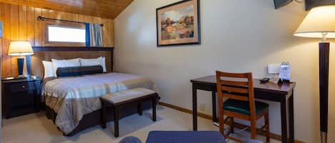 Une chambre à coucher avec un lit, un bureau, une chaise, une lampe et un tableau au mur.
